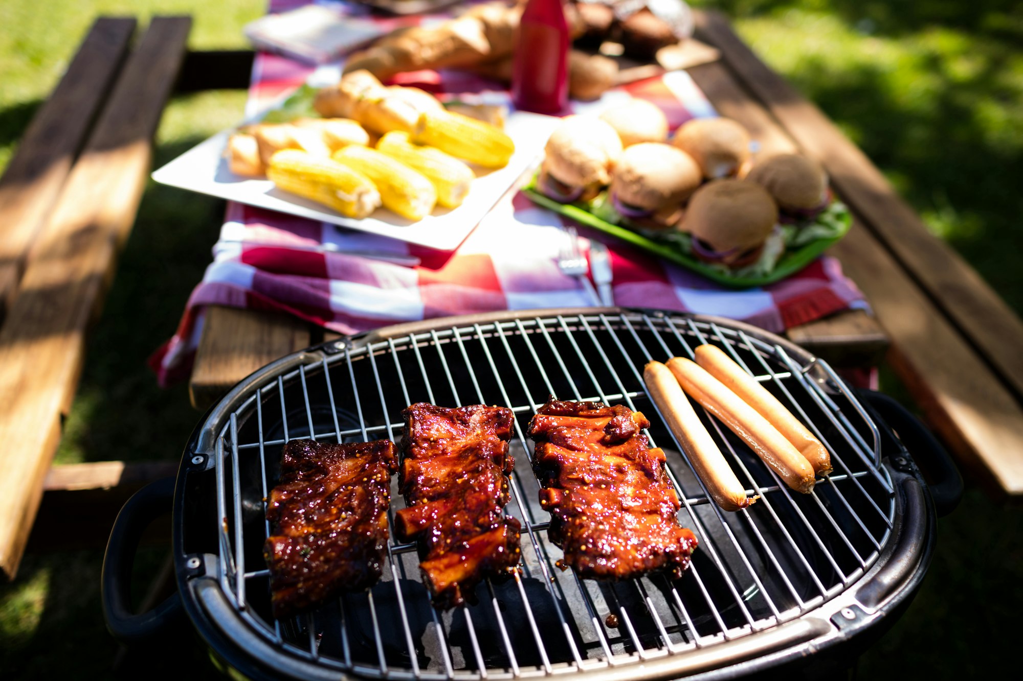 Barbeque with buns and corn on table in park